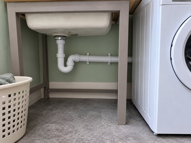 A kitchen sink waste trap and pipework being cleared under the unit
