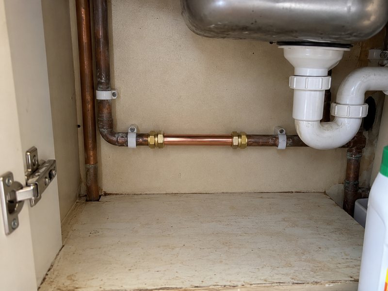 A leaking pipe joint under a sink with water on the cabinet base
