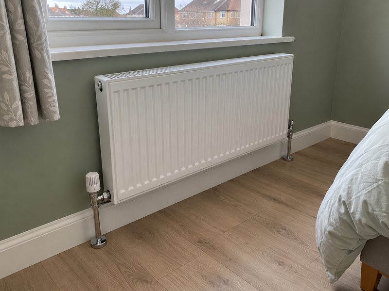 A radiator fitted under a window with a thermostatic valve on the pipework