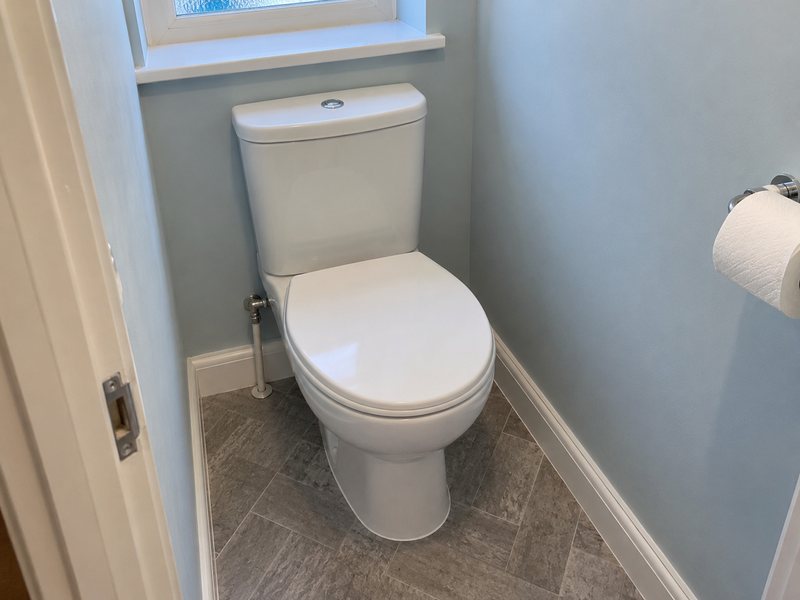 A close-coupled toilet fitted in a cloakroom with the cistern and supply pipework visible